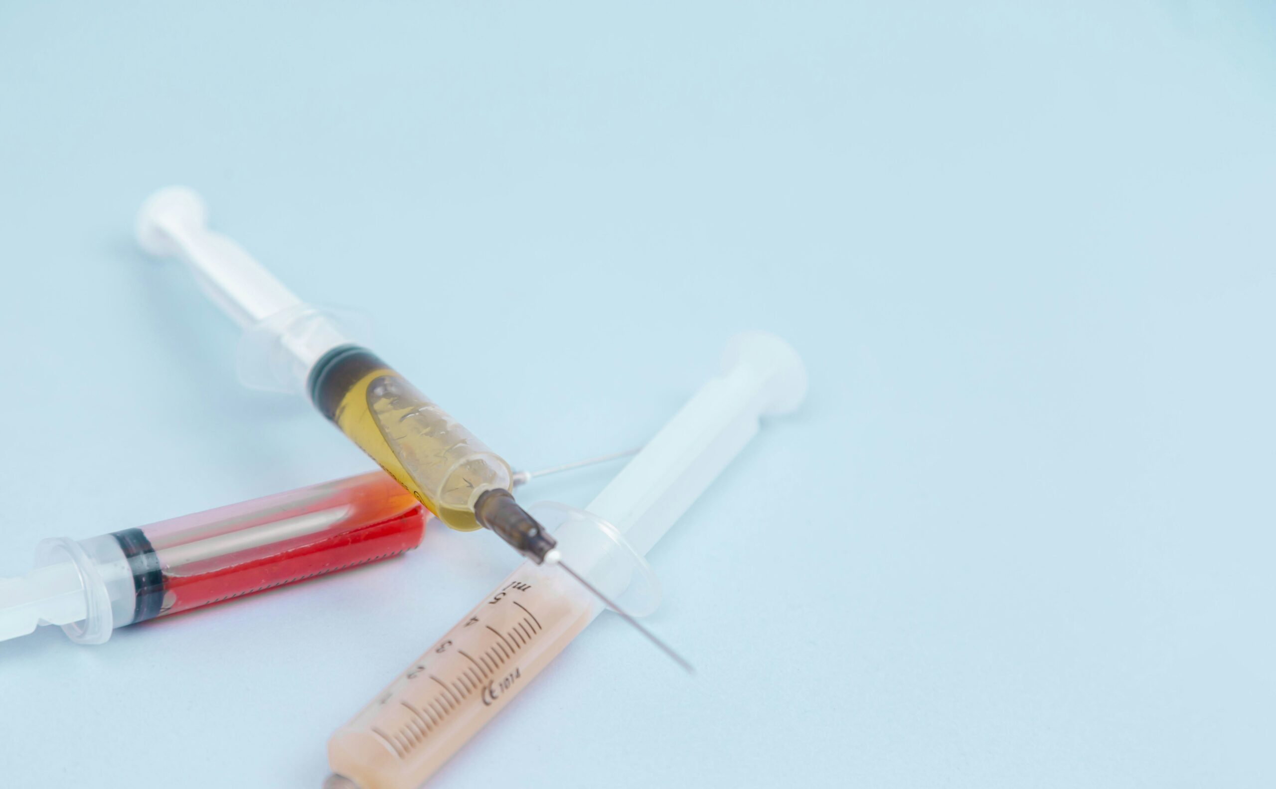 Syringes with different medicines in yellow, red, orange and transparent colors lie on a blue background. The medicine. Vaccine. Covid 19. Coronovirus. An injection. Drugs. The close plan. Top view.